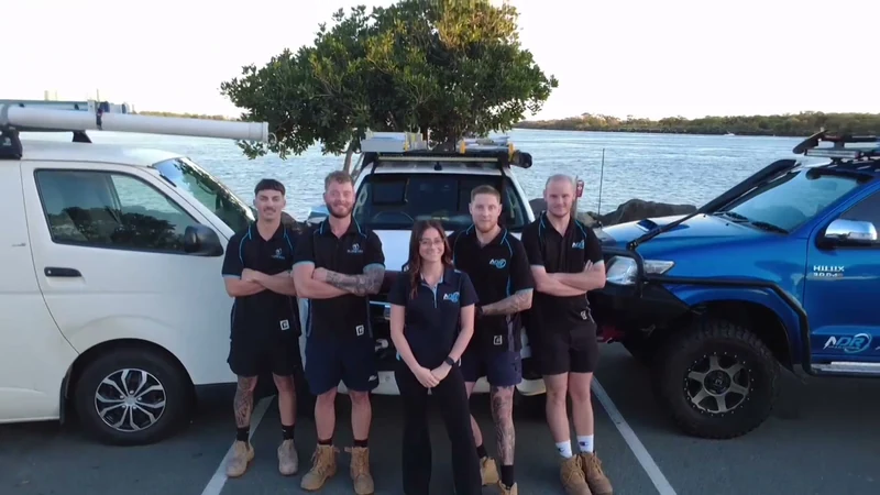 Five NDR team members smiling beside their work vehicles on the Gold Coast