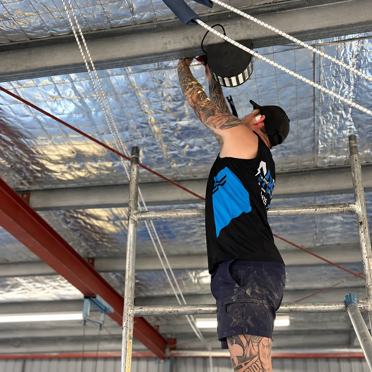 An NDR electrician installing lighting in a gym